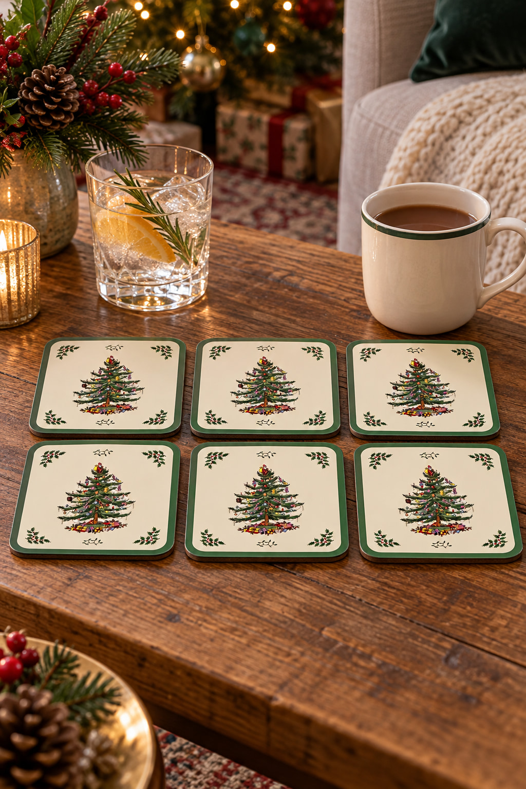 Six cream Christmas Tree coasters with green borders, arranged in two rows of three on a wooden coffee table beside drinks.