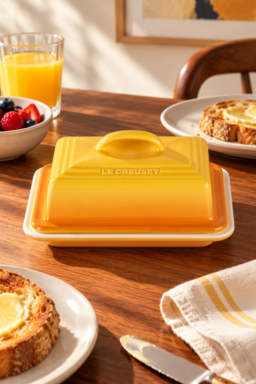 A golden-yellow rectangular butter dish with an arched lid handle, on a walnut breakfast table with toast and berries.