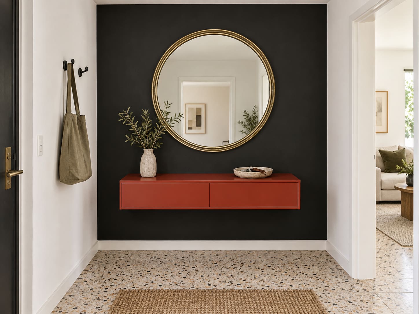 A black end wall gives this pale hallway a clear destination. A round brass mirror and a floating red drawer turn one compact wall into a useful arrival point.