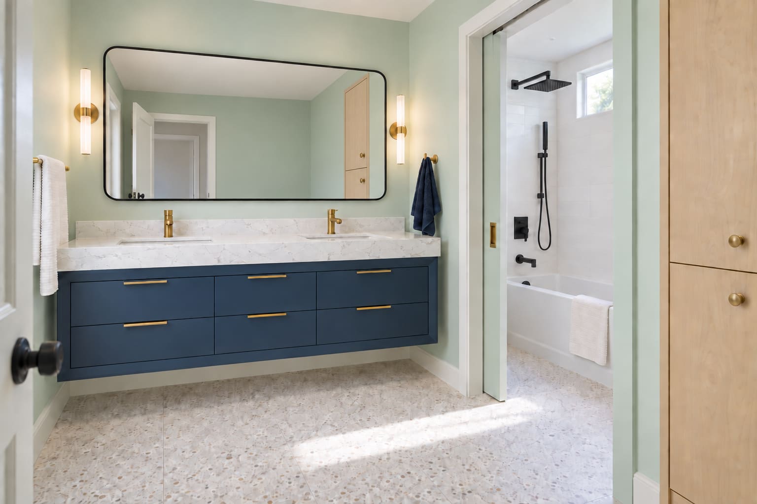 Mint family bathroom with a navy double vanity, wide black-framed mirror and a tub-shower behind a solid pocket door.