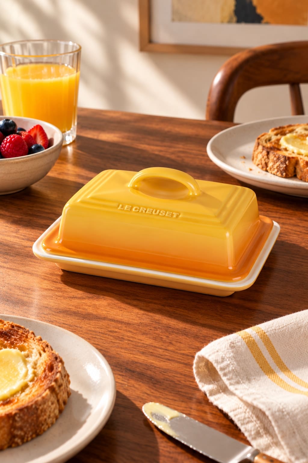 A golden-yellow rectangular butter dish with an arched lid handle, on a walnut breakfast table with toast and berries.
