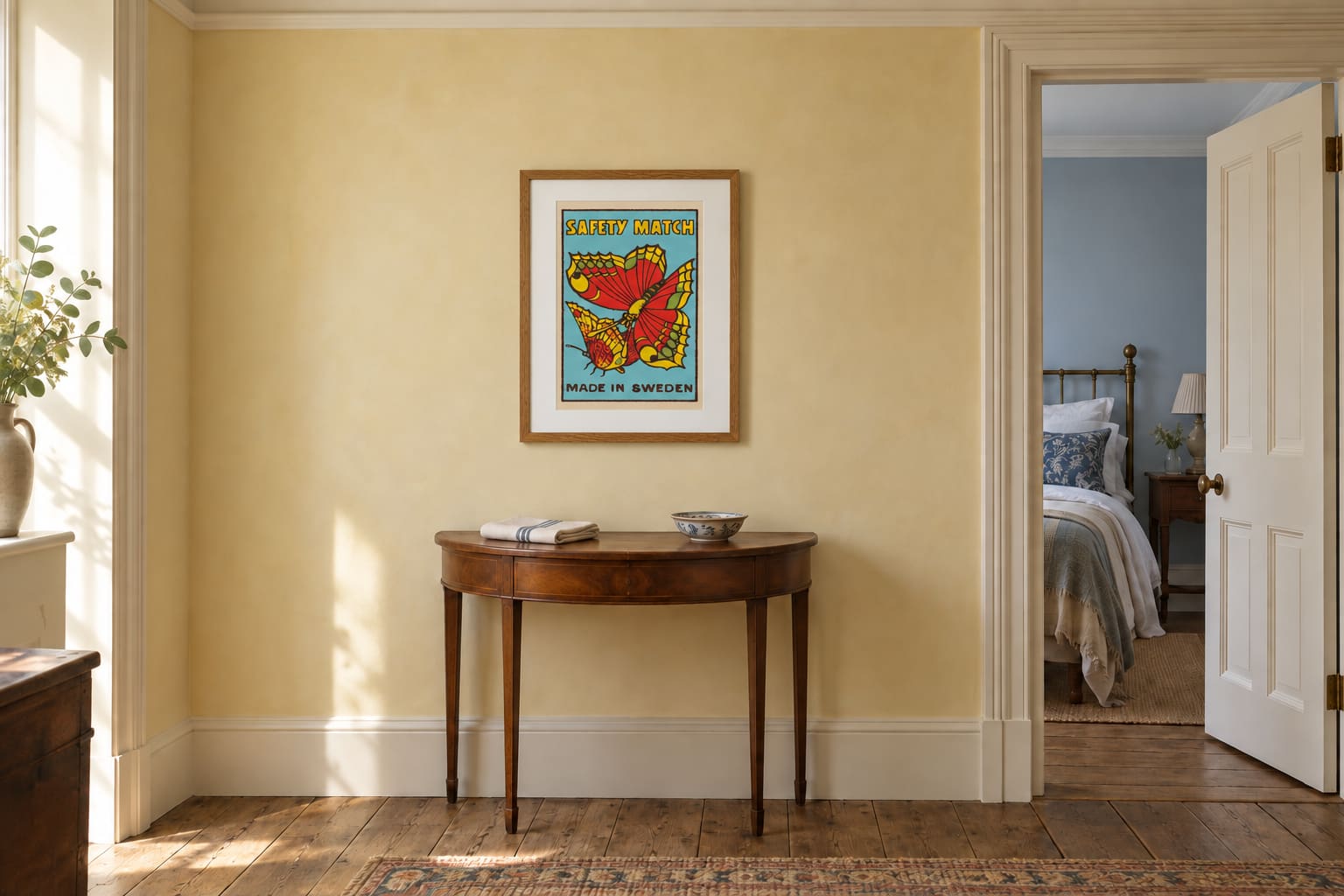 A red and turquoise Butterfly matchbox-label print above a mahogany console on a pale yellow landing.